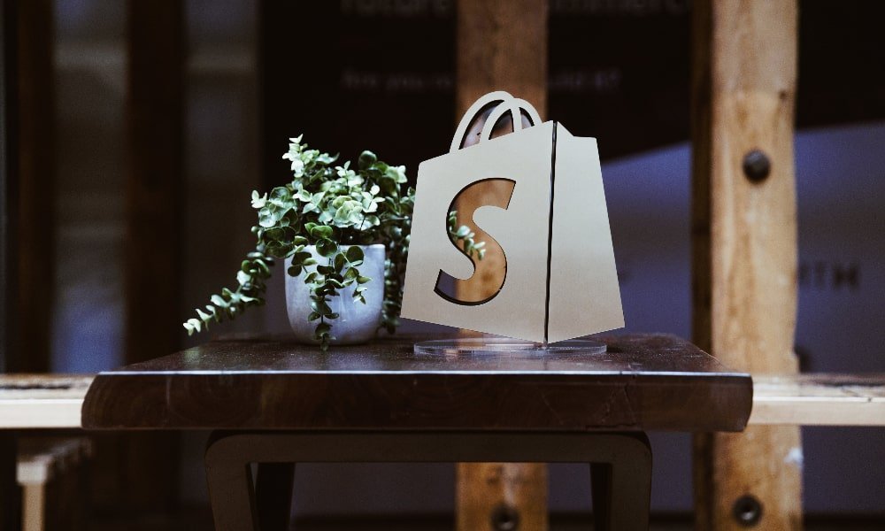 Urezani shopify logo na stolu kraj vazee