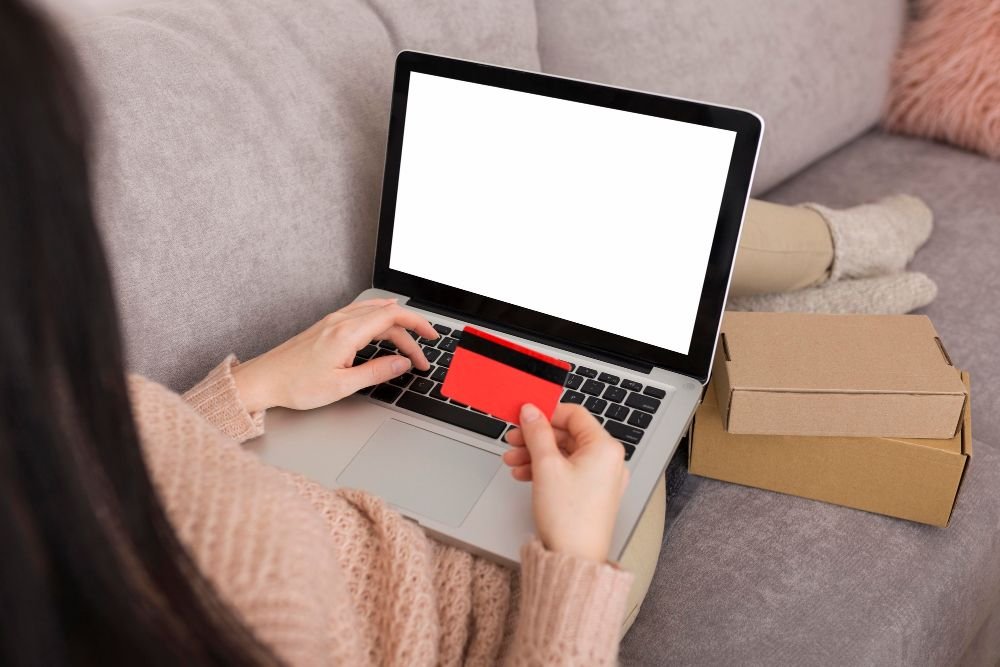 žena leži na kauču drži kreditnu karticu i laptop sa bijelim ekranom