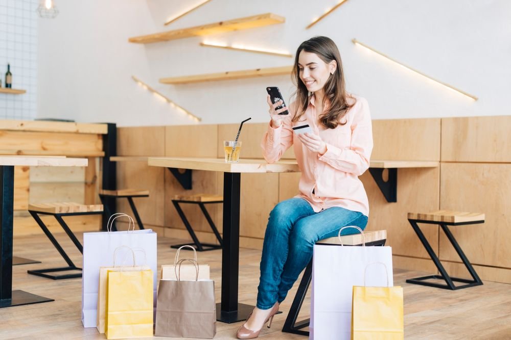 žena sjedi za stolom sa mobitelom i kreditnom karticom i shopping vrećama